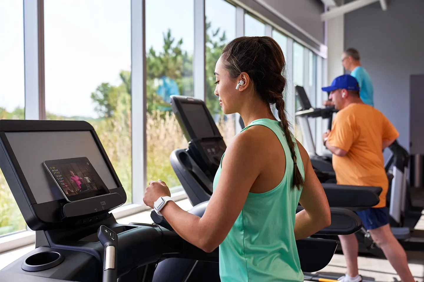 Woman exercising on treadmill at a gym with others in the background.